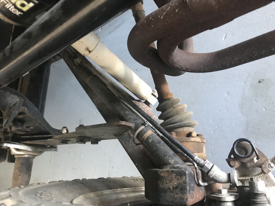 Underside of vehicle suspension with rusty exhaust pipes, shock absorber, and tire.
