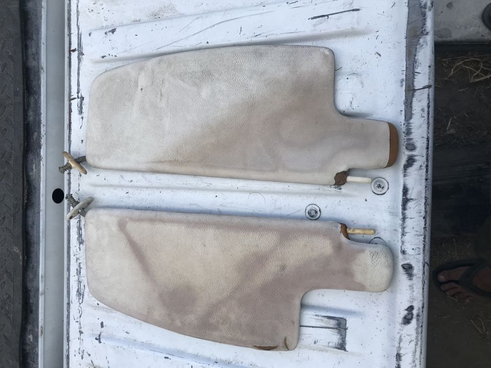 Two beige sun visors with wooden pegs on a white surface.