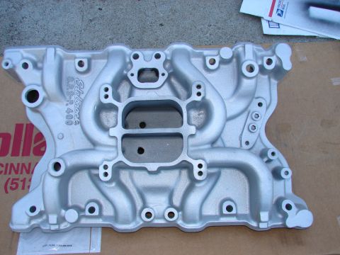 1973 Ford Ranchero - A silver Edelbrock Performer RPM dual plane intake manifold is shown from a top-down perspective, resting on a cardboard box. The manifold…