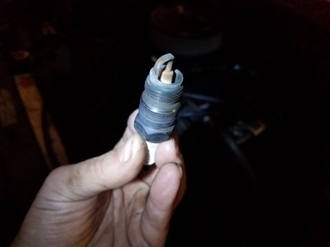 1985 Ford Bronco - A hand holds a used spark plug with a bent electrode against a dark, out-of-focus background.