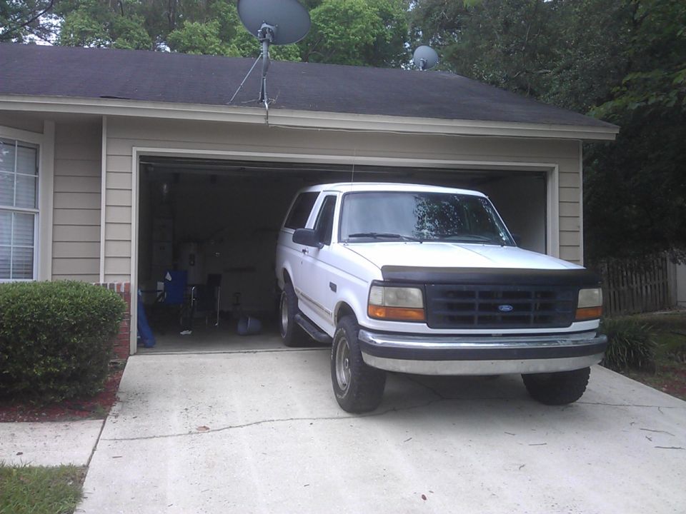 White Ford Bronco parked in front of an open garage.