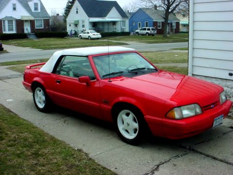 1992 Ford Mustang - A red convertible with a white top is parked in front of a suburban house.