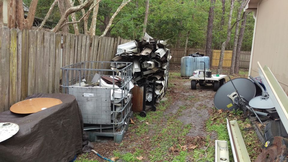 Backyard scene with scrap metal, siding, satellite dishes, and cages.