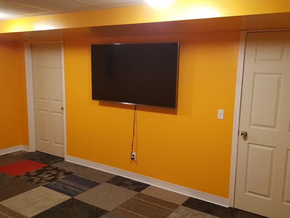 Flat-screen TV on orange wall with two white doors and patterned carpet.