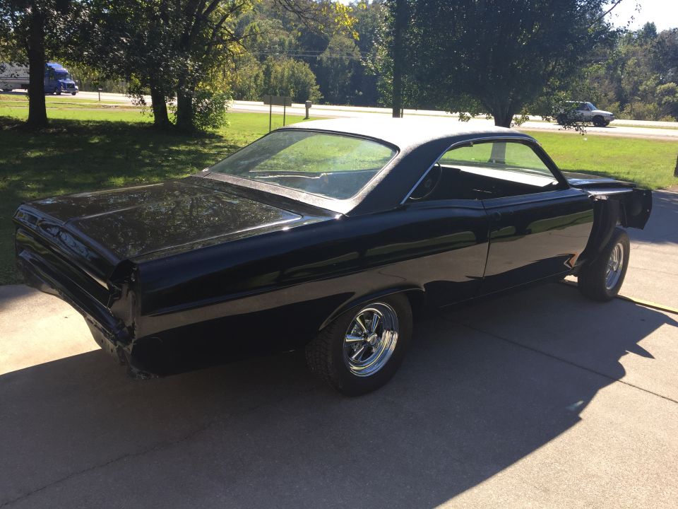 Black 1967 Mercury Cyclone coupe with white roof, chrome wheels, parked on concrete.