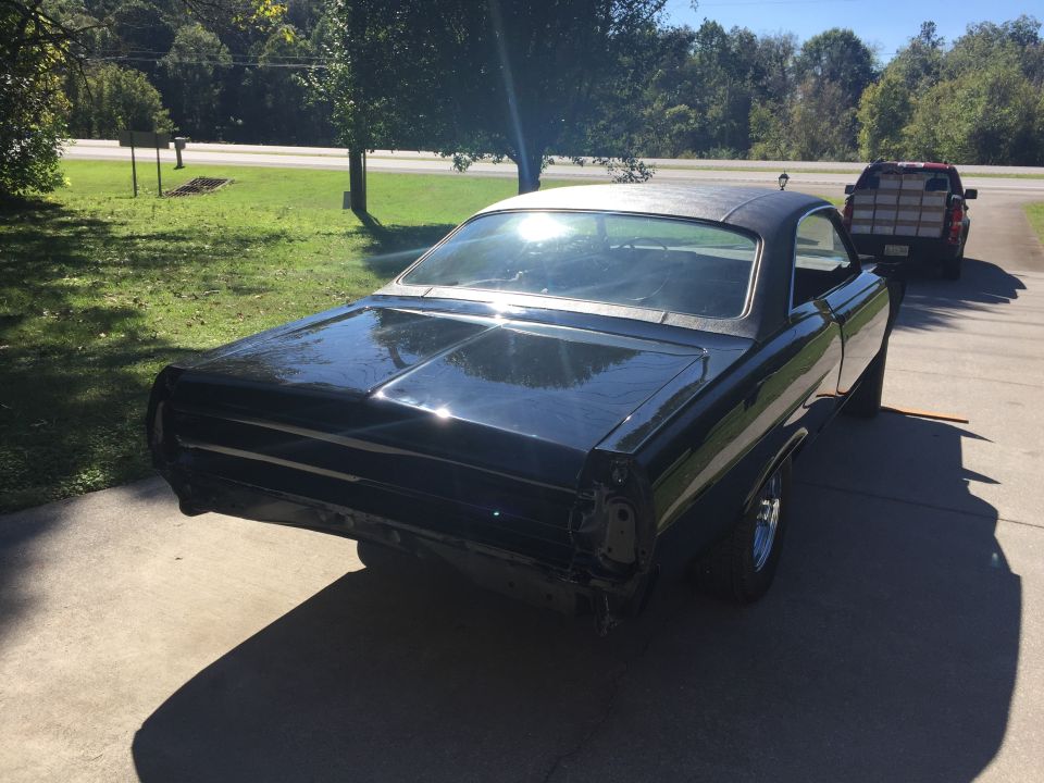Black classic coupe, rear passenger side view, parked on concrete driveway.