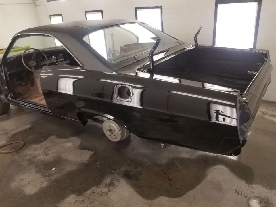 Black coupe with trunk open and driver's door removed in a workshop.