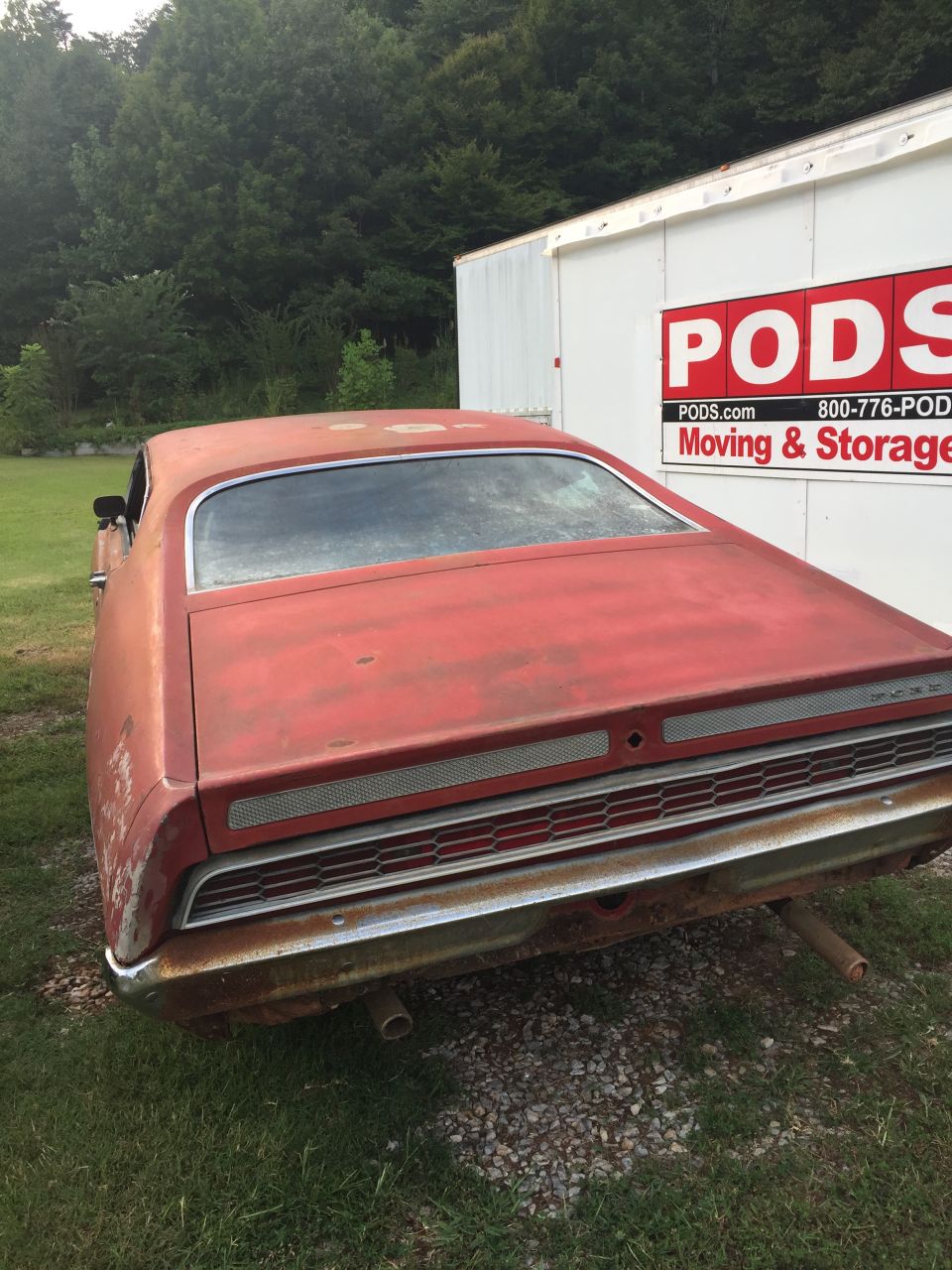 Faded red 1970 Ford Torino rear view parked next to a PODS storage container.