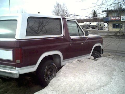 1983 Ford Bronco - Maroon and white Ford Bronco is stuck in a pile of snow.