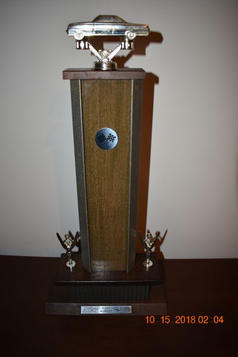 1996 Ford Bronco - A trophy with a silver car on top sits on a wooden base. The trophy has a wooden middle section with a checkered flag emblem and two small…