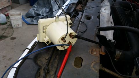 1985 Ford Bronco - A close-up view of a white, cylindrical automotive component, possibly a voltage regulator or relay, with electrical testing probes attache…