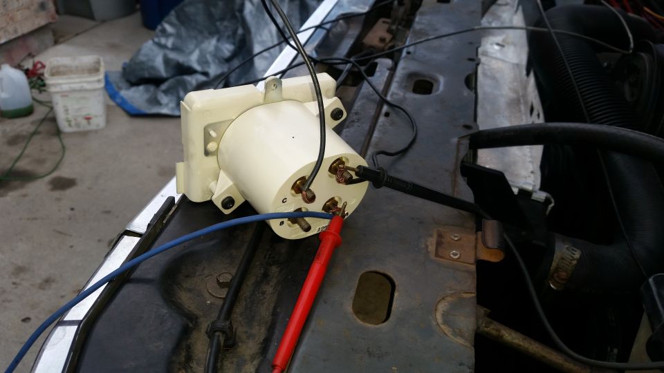 Automotive voltage regulator or relay with testing probes attached in an engine bay.