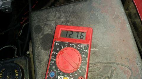 1985 Ford Bronco - A red digital multimeter displays a reading of 12.76 volts, positioned on a dusty, grey metal surface that appears to be part of a vehicle'…