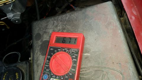 1985 Ford Bronco - A red digital multimeter displays a reading of 6.71 while resting on a weathered metal surface, likely in an engine bay.