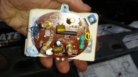 1985 Ford Bronco - A hand holds a circuit board with various electronic components, including resistors, capacitors, and connectors. The circuit board appears…