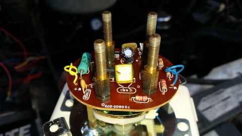 1985 Ford Bronco - A close-up view of a red circuit board with several components, including capacitors, resistors, and four threaded bolts, mounted on top of…