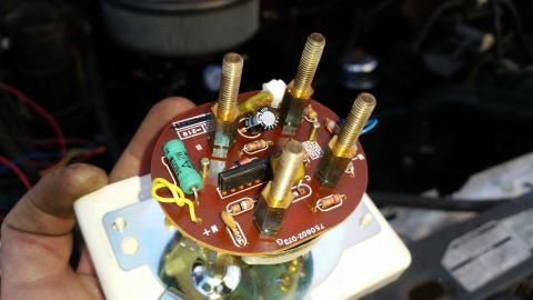 1985 Ford Bronco - A close-up view of the back of a gauge cluster circuit board, held by a hand. The board has several brass screw terminals, resistors, a cap…