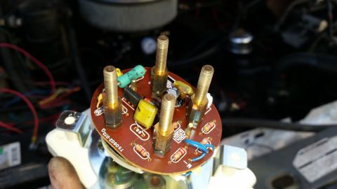 1985 Ford Bronco - A close-up view of a circuit board with several brass threaded posts, resistors, and capacitors. The circuit board is mounted on a white pl…