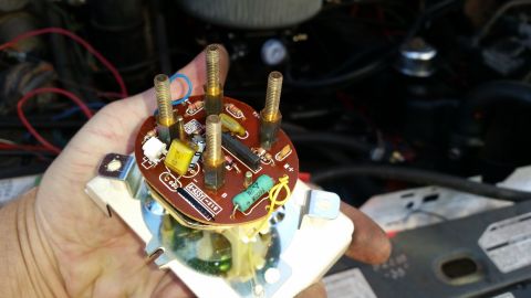 1985 Ford Bronco - A hand holds a circuit board with brass terminals, resistors, and capacitors, likely from a vehicle's dashboard gauge cluster. The backgrou…
