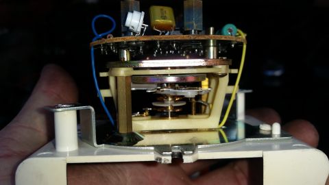 1985 Ford Bronco - A close-up view of the internal mechanism of what appears to be an electronic device, possibly a clock or timer, being held by a hand. The…