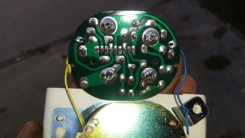 1985 Ford Bronco - A close-up view of the back of a green circuit board with silver solder points and two wires, a yellow one and a blue one. The circuit boar…