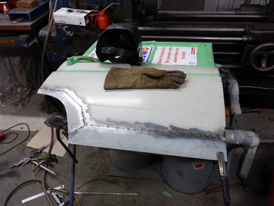 Car door panel being welded, with welding mask and gloves on top.