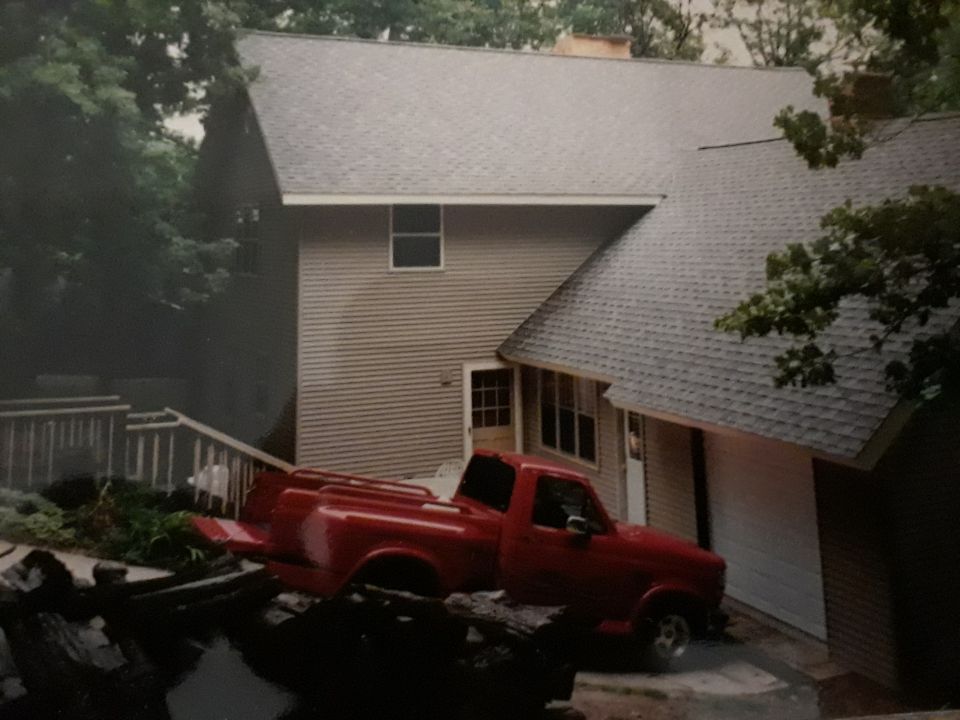 Red pickup truck parked on a deck next to a house