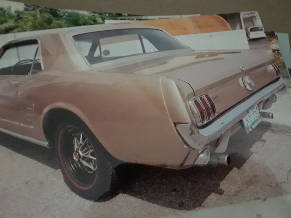 Rear driver's side quarter view of a metallic gold classic coupe, possibly a Ford Mustang.