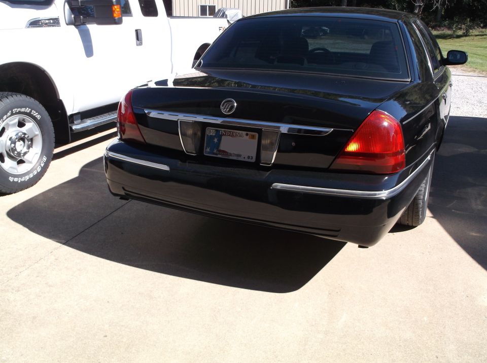 Black Mercury Grand Marquis rear view with Indiana license plate parked next to a white pickup truck.
