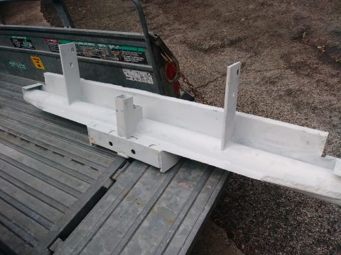 1996 Ford Bronco - A white painted steel bumper or frame component with two upright brackets is resting on a grey metal trailer bed. The component has a recta…