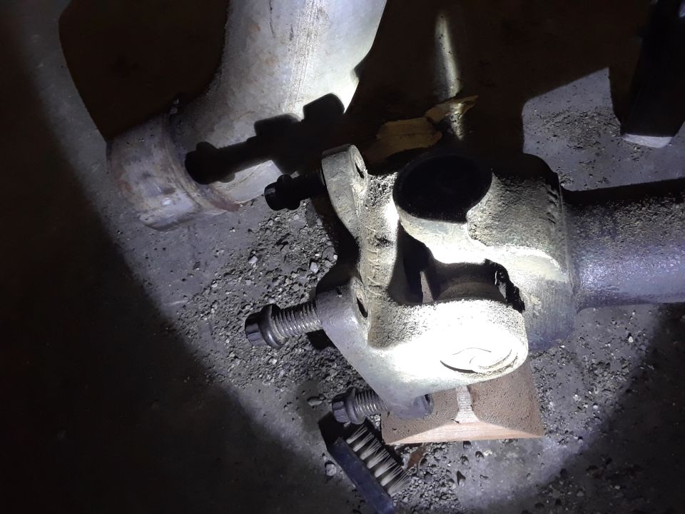 Close-up of a metal u-joint and driveshaft parts on gravel.