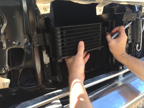 1978 Ford Bronco - A person is holding a black transmission cooler in front of a vehicle's radiator and using a marker to mark a location on the cooler. The v…