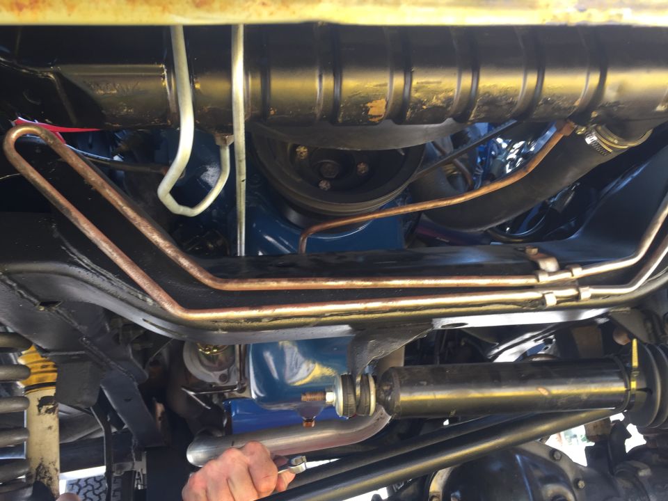 Underneath view of vehicle engine bay with copper lines, suspension, and blue engine block.