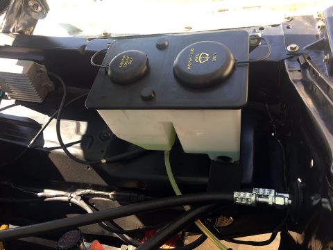 1978 Ford Bronco - The image shows a close-up view of the engine bay of a vehicle, focusing on the windshield washer fluid reservoir and the radiator coolant…