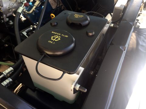 1978 Ford Bronco - A close-up view of the washer fluid reservoir and radiator coolant cap on a black engine cover. The washer fluid cap has a yellow windshiel…