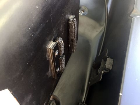 1978 Ford Bronco - Close-up view of two metal brackets with rubber padding attached to a black panel, likely part of a vehicle's interior or undercarriage.