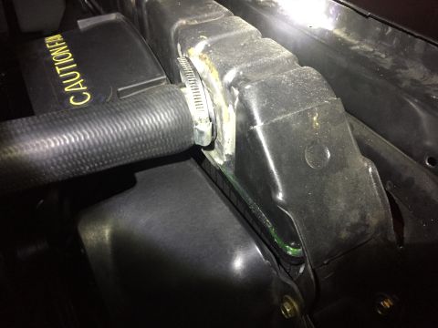 1978 Ford Bronco - A close-up view shows a black radiator hose secured with a metal clamp to a black plastic radiator shroud. Yellow text reading "CAUTION FAN…