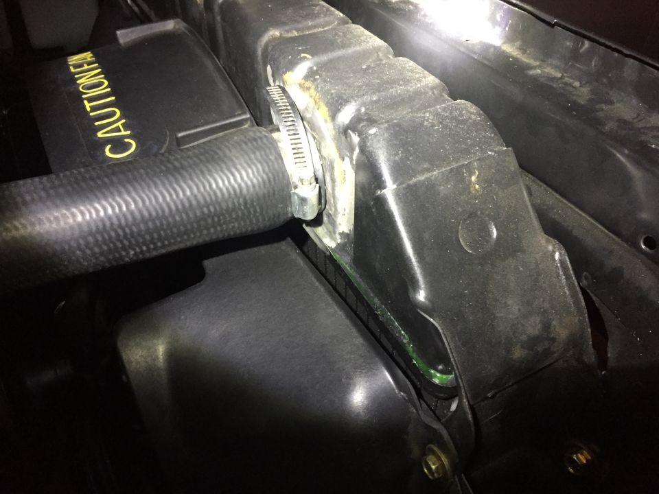 Radiator hose clamped to a black plastic shroud with yellow caution text.