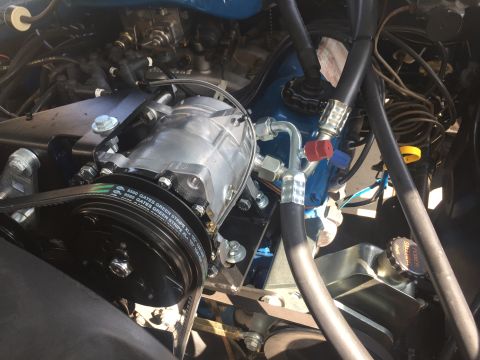 1978 Ford Bronco - Close-up view of a vehicle's engine bay, focusing on the air conditioning compressor and associated hoses. The compressor is a silver, cyli…