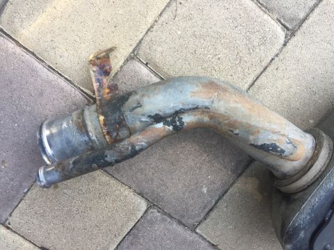 1978 Ford Bronco - A rusted and weathered metal exhaust pipe component is shown lying on a paver stone surface. The pipe has a curved shape and shows signs of…