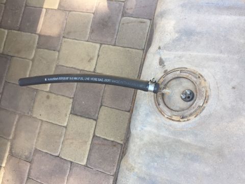 1978 Ford Bronco - A close-up view of a black fuel line hose with text printed on it, connected to a fuel tank opening with a clamp. The fuel tank is resting…