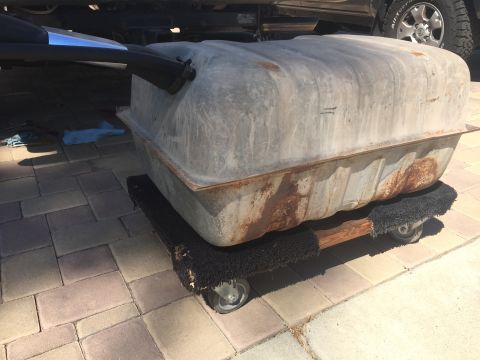 1978 Ford Bronco - A large, rusty metal fuel tank is mounted on a wooden dolly with wheels. The dolly is placed on a paved patio, with a vehicle's undercarria…