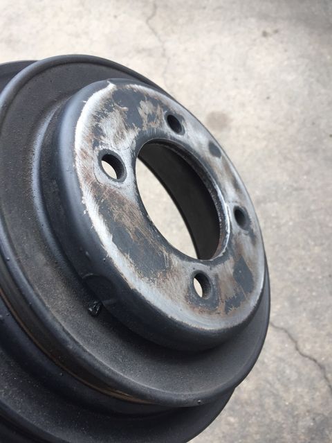1978 Ford Bronco - A close-up, angled view of a worn, black metal pulley or brake rotor with three bolt holes visible. The surface shows significant wear and…