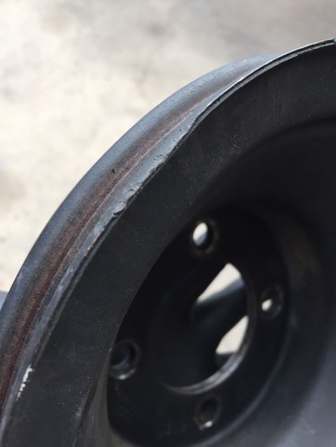 1978 Ford Bronco - A close-up, angled view of a dark-colored, possibly cast iron, pulley or wheel rim. The outer edge shows signs of wear and rust, with some…