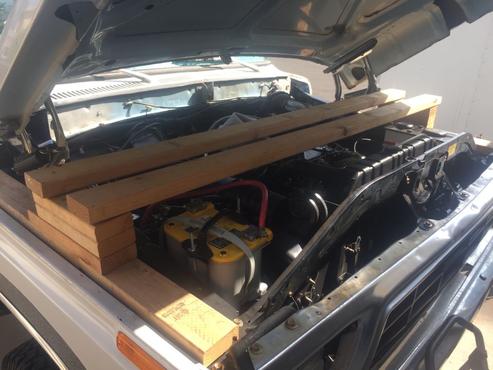 Wooden planks stacked on fender over engine bay of classic vehicle with yellow Optima battery.