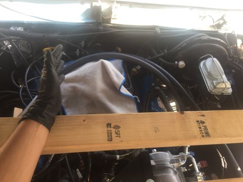 1978 Ford Bronco - A gloved hand reaches into the engine bay of a vehicle, holding a rag over a blue component. A wooden board with text is positioned across…