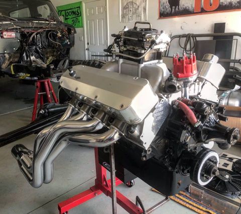 1979 Ford Bronco - A polished V8 engine with chrome headers and a red distributor cap is mounted on a red engine stand in a garage. A partially disassembled v…