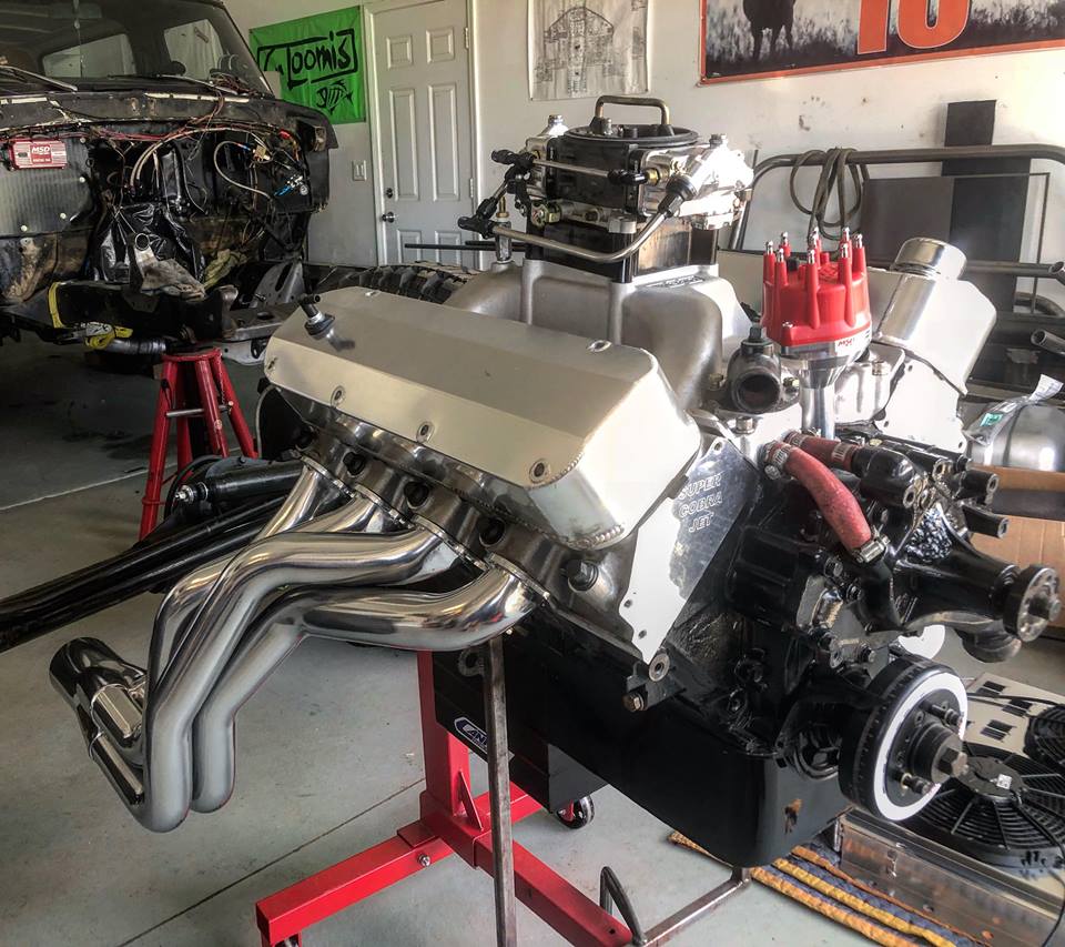 Polished V8 engine with chrome headers on a red engine stand.