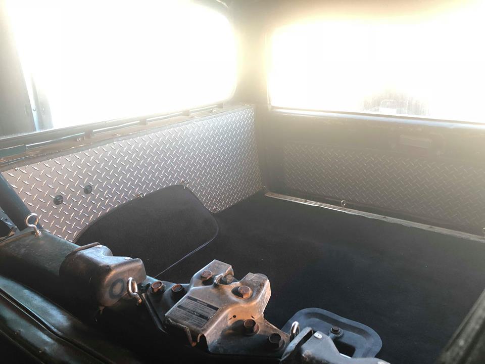 Interior of a vehicle cargo area with diamond plate walls and carpeted floor, showing a trailer hitch.