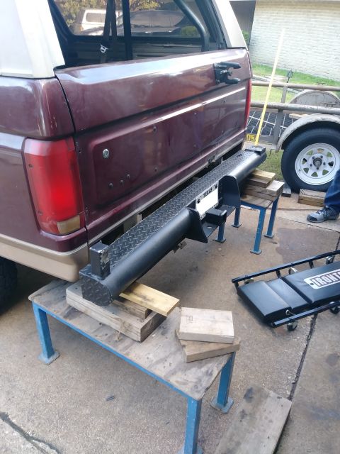 1996 Ford Bronco - The rear of a maroon Ford Bronco is shown, modified with a black diamond plate bumper. The vehicle is supported by wooden blocks on a blue…